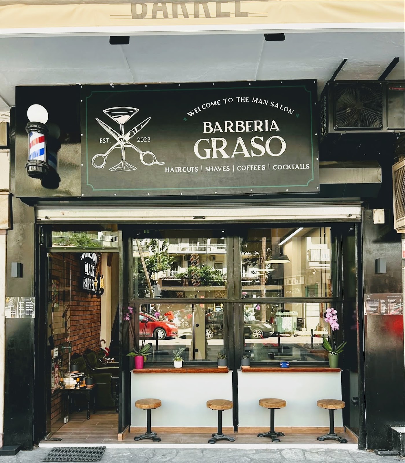 Η πρόσοψη της Barberia Graso στην Παπαναστασίου 3, με την πράσινη ταμπέλα και τα ξύλινα σκαμπό στη βιτρίνα